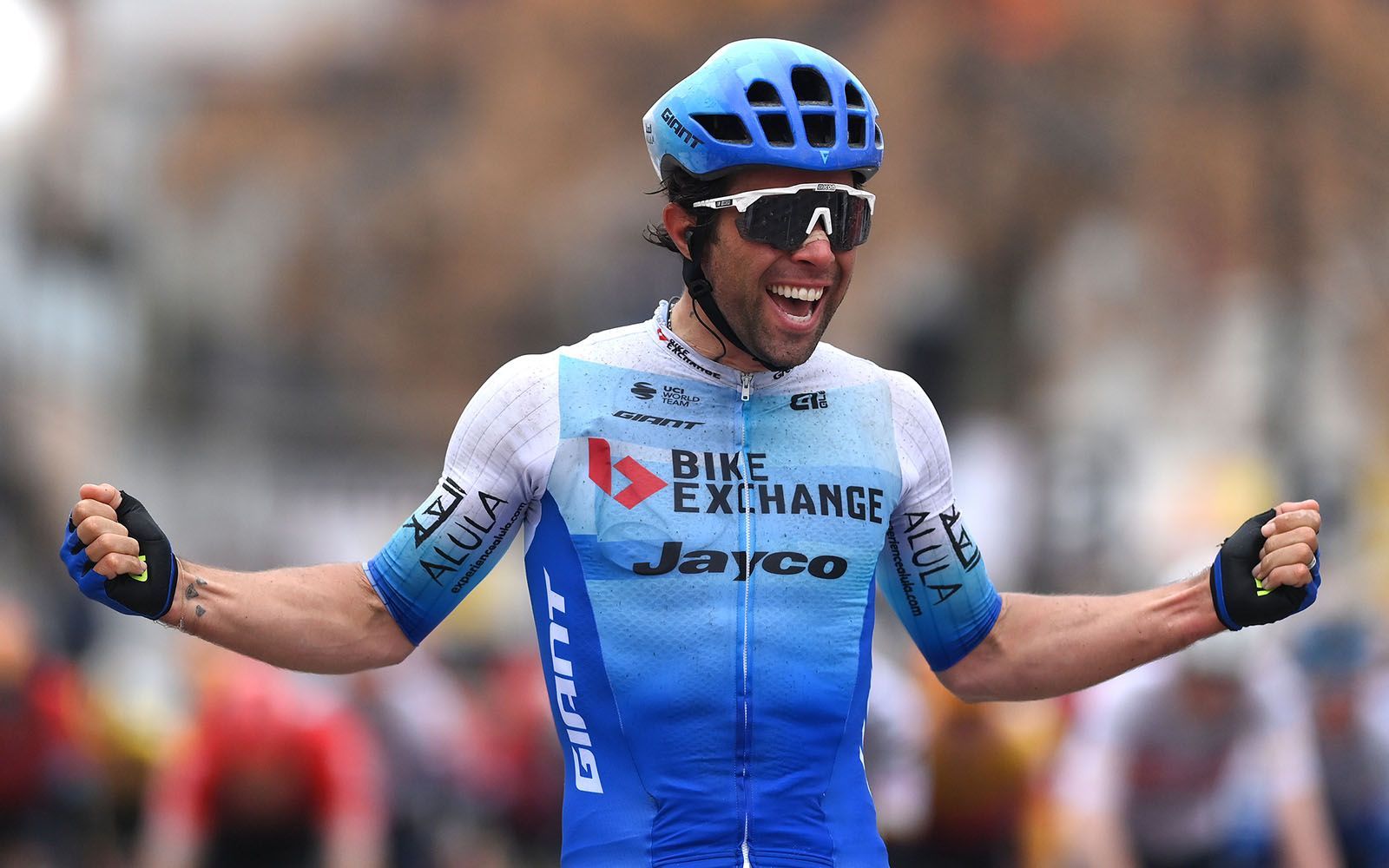 Cyclist in blue jersey with arms raised, celebrating victory.