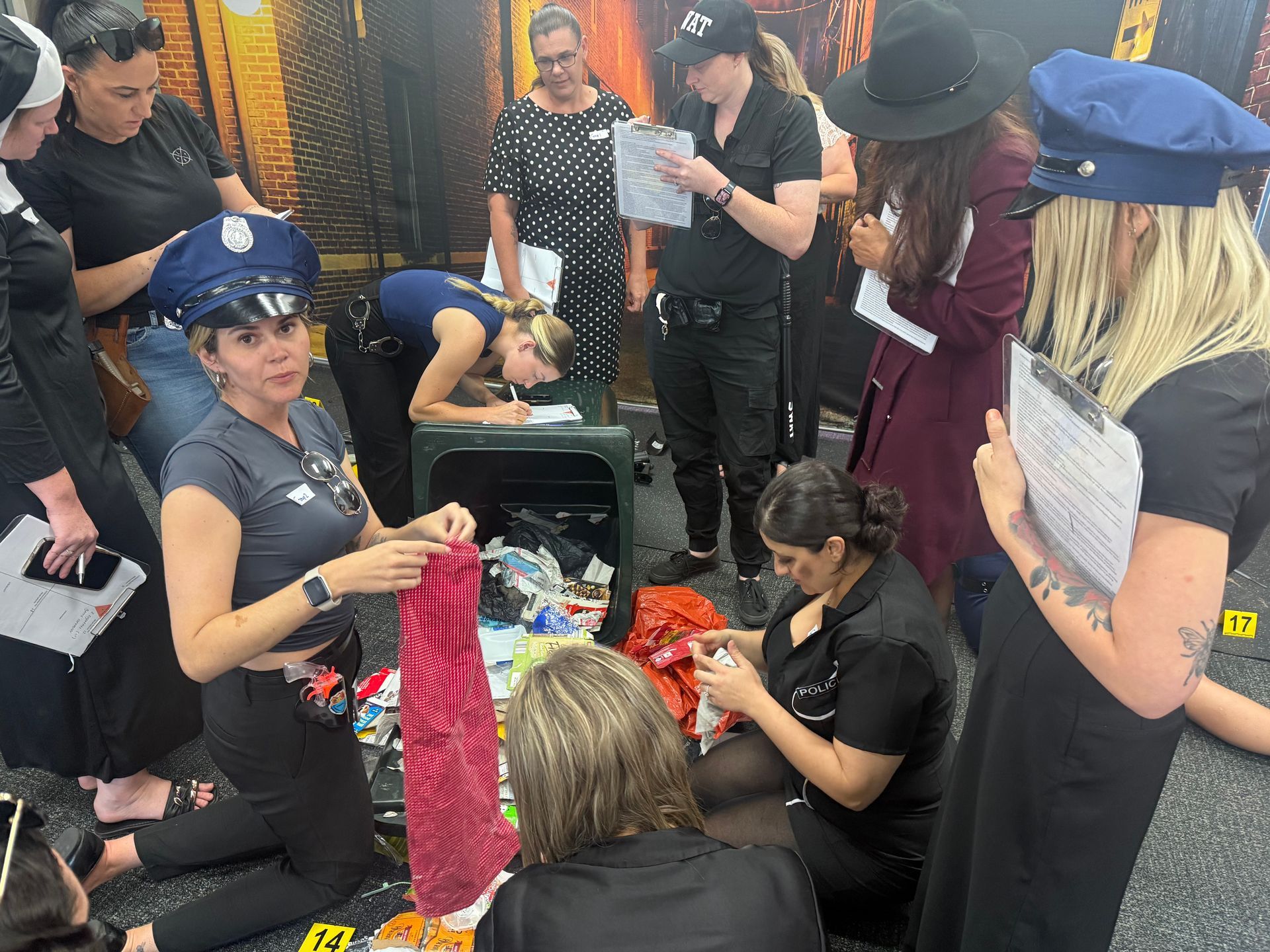 People in a room examining items, some dressed in police attire, possibly at a crime scene investigation.