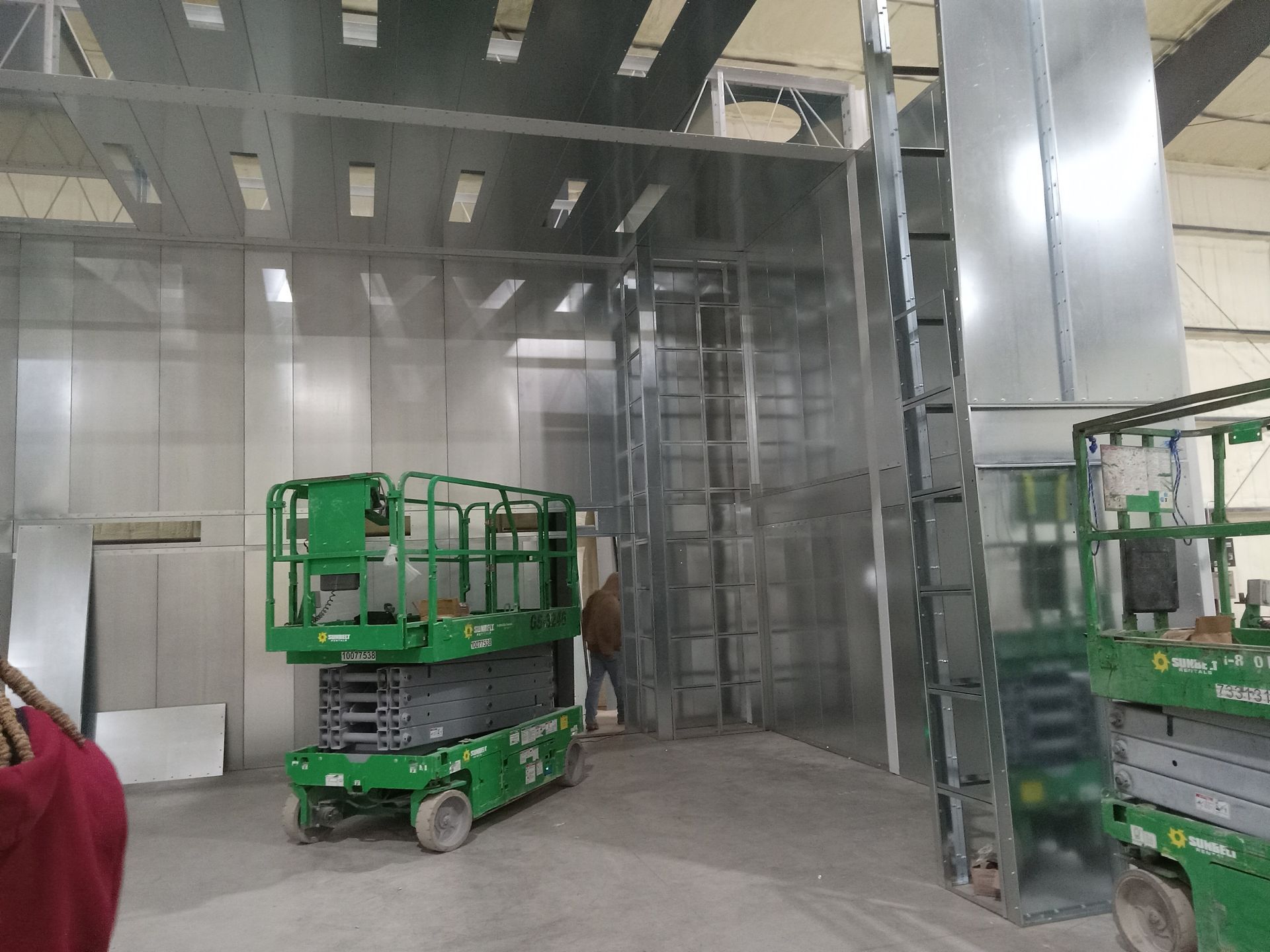 A green scissor lift is parked in a warehouse.