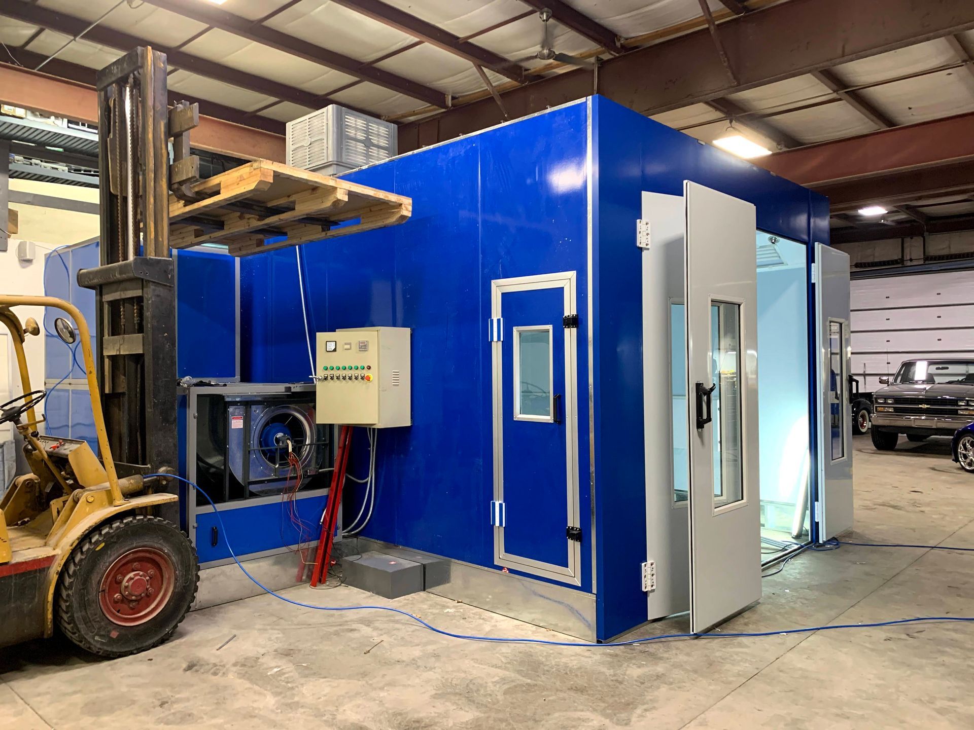 A forklift is parked in front of a blue paint booth in a garage.