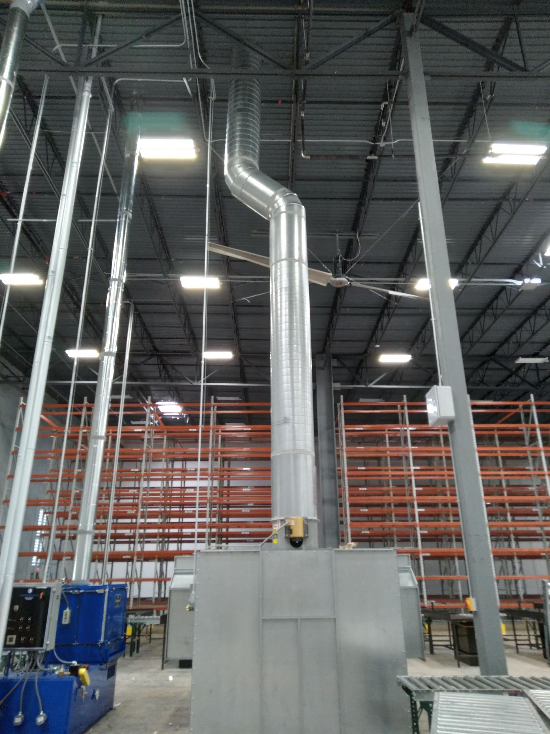 A large warehouse with lots of shelves and a large pipe coming out of the ceiling.
