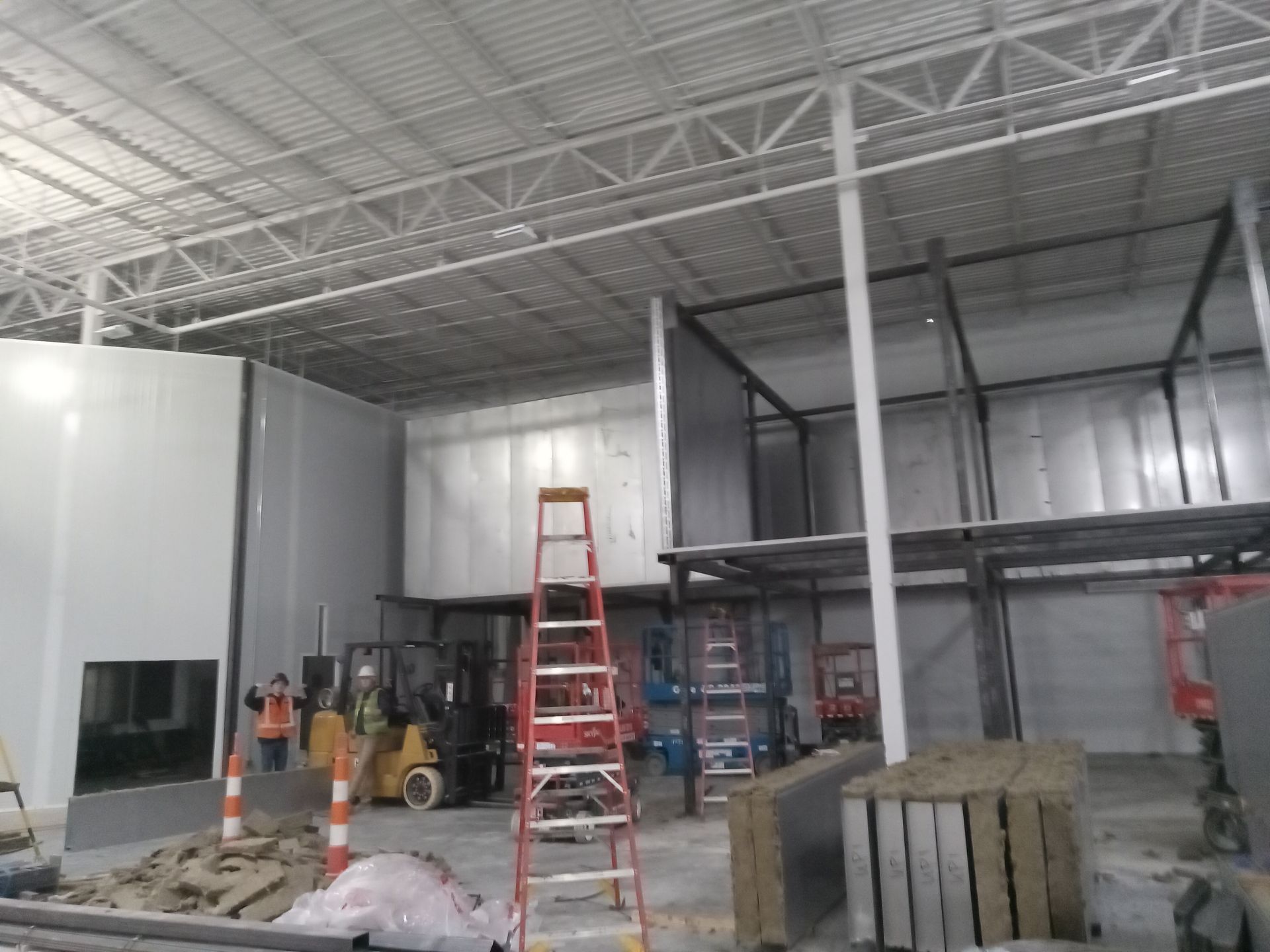 A large warehouse with a forklift and a ladder in the middle of it.
