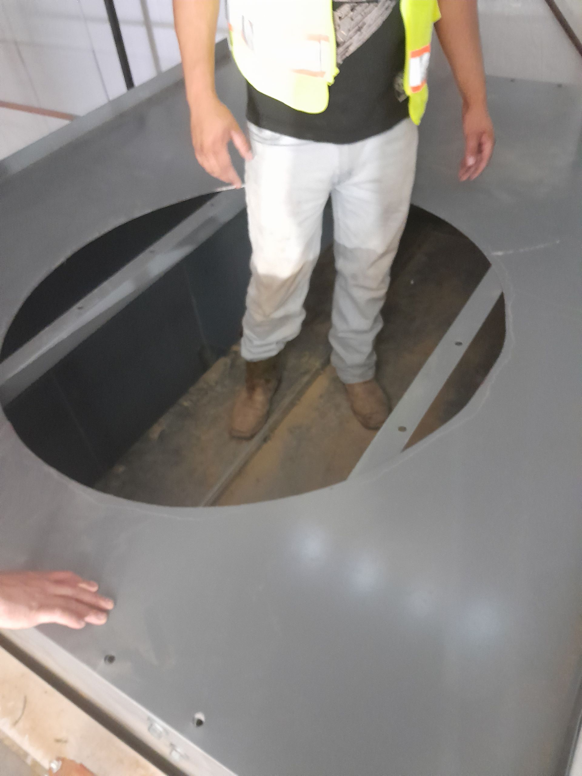 A man in a yellow vest is standing in a circular hole