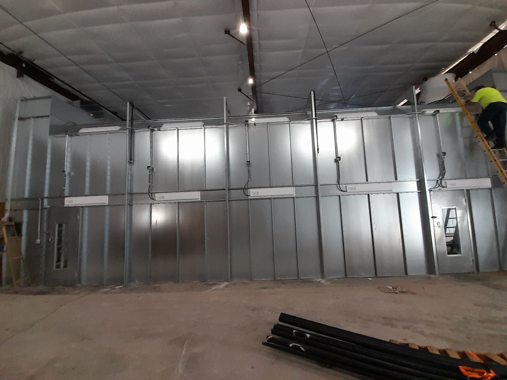 A man is standing on a ladder in front of a large metal wall.