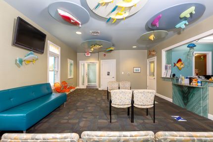 Colorful children's waiting room with teal couch, fish wall decor, TV, and small chairs.