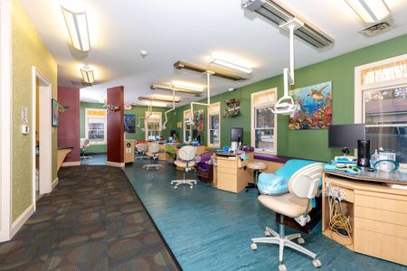 Colorful office workspace with desks, chairs, computers, and fluorescent ceiling lights.