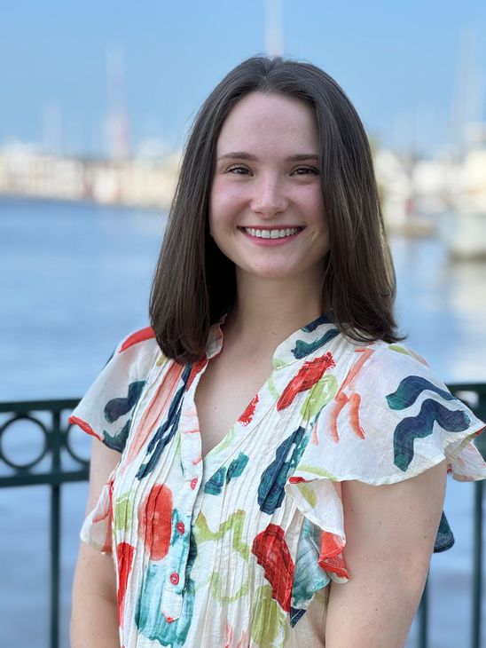 Smiling person in a white floral dress standing against a dark studio backdrop