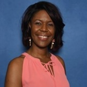 A woman wearing a pink top and earrings smiles for the camera