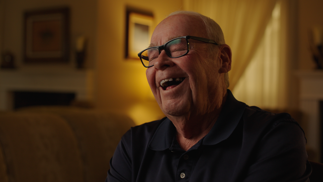 Smiling bald man in glasses sitting on a couch in a warmly lit living room