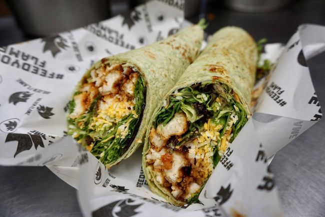 Two halves of a chicken and salad wrap served on branded white paper.