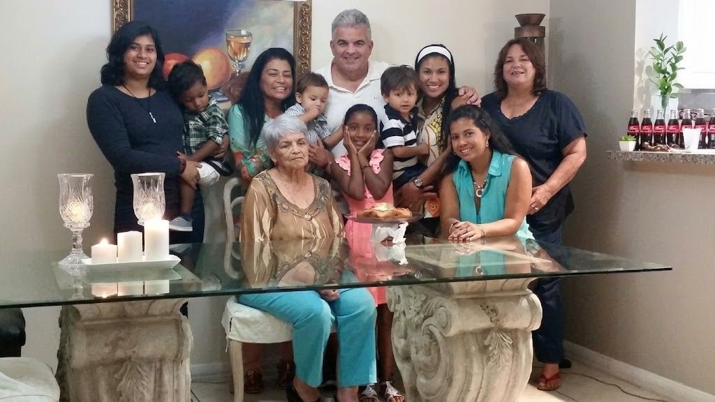 Family group posing around a glass dining table in a living room, with candles and a red cake centerpiece.