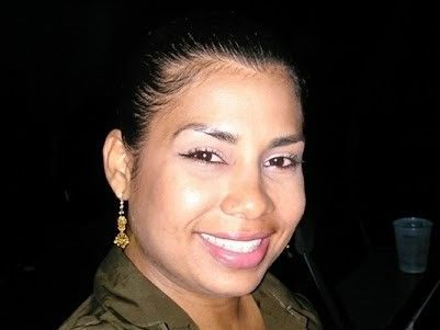 Smiling woman with pulled-back hair and gold earrings against a dark background