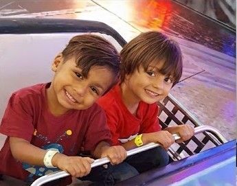 Two smiling children in red shirts riding together on a amusement ride vehicle