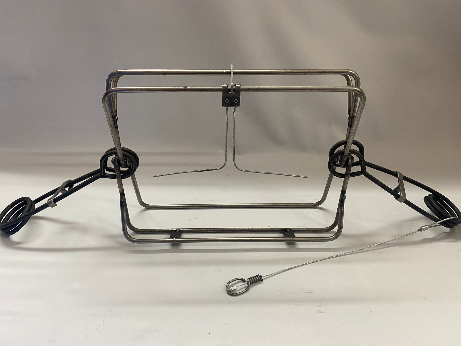 Steel animal trap, open and ready, with springs and attached cable.