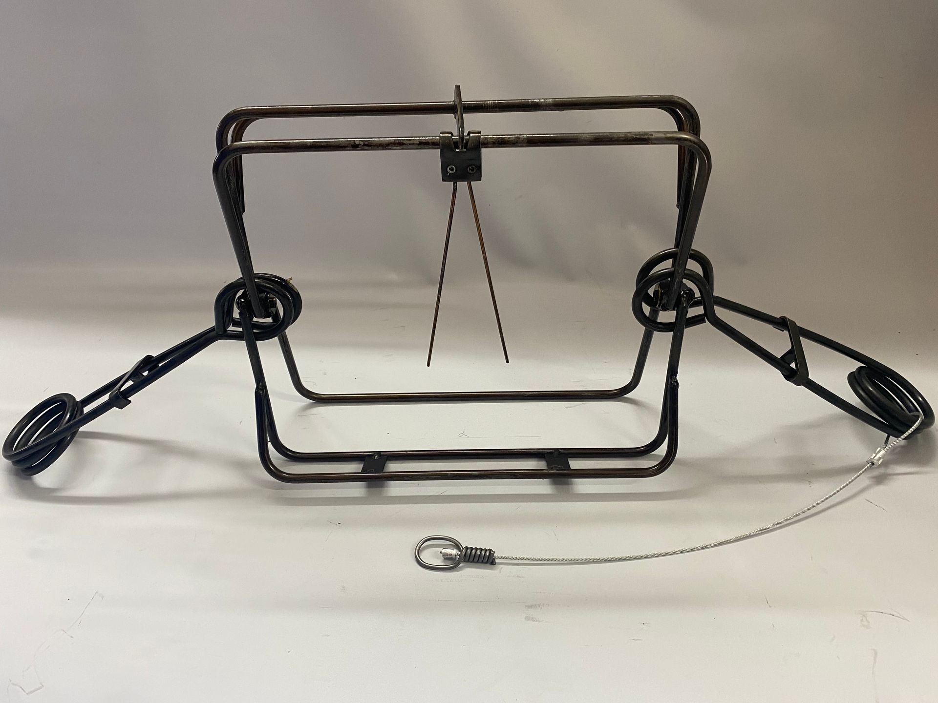 A metal animal trap with a square frame, spring-loaded arms, and a wire cable.