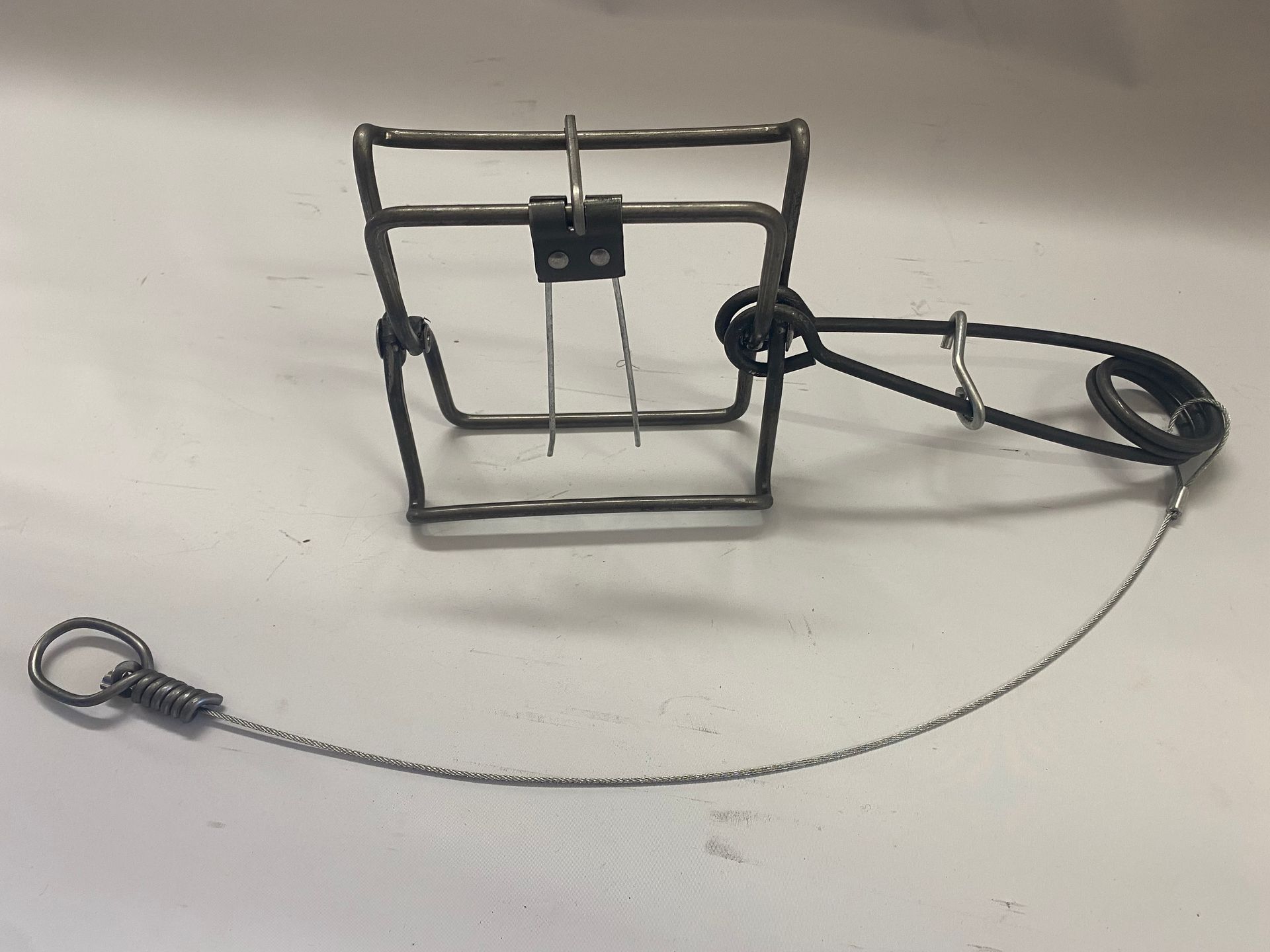 Metal animal trap with a spring and chain, on a white surface.