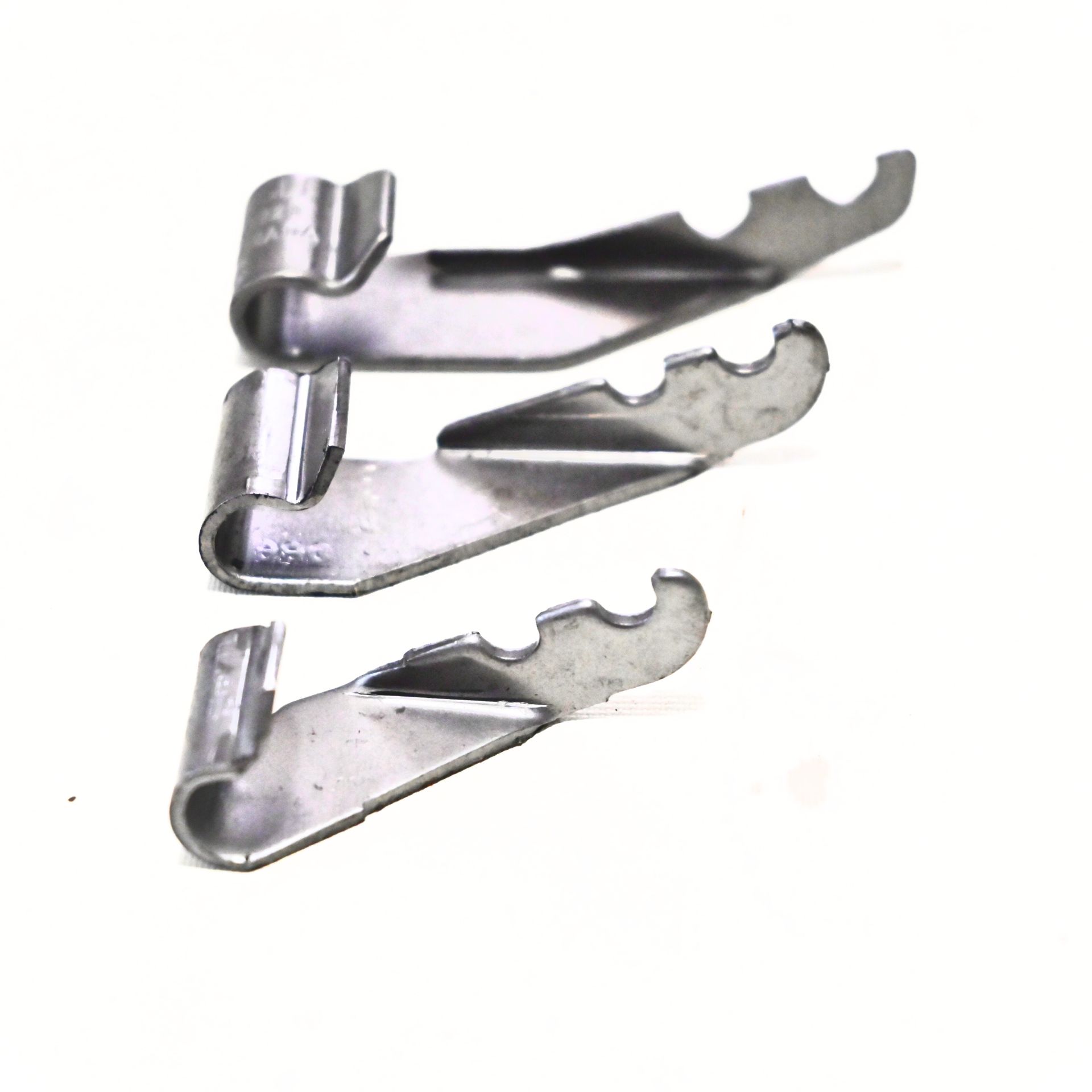 Trois clips métalliques avec une extrémité recourbée et trois encoches sur le bord.