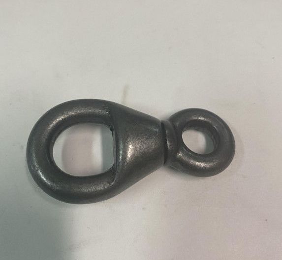 Un œillet métallique et un connecteur pivotant en forme de larme sur une surface blanche.