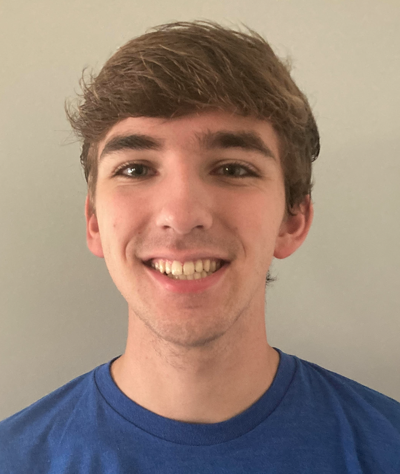 A person with short, brown hair wearing a blue shirt smiles warmly against a plain, light gray background.