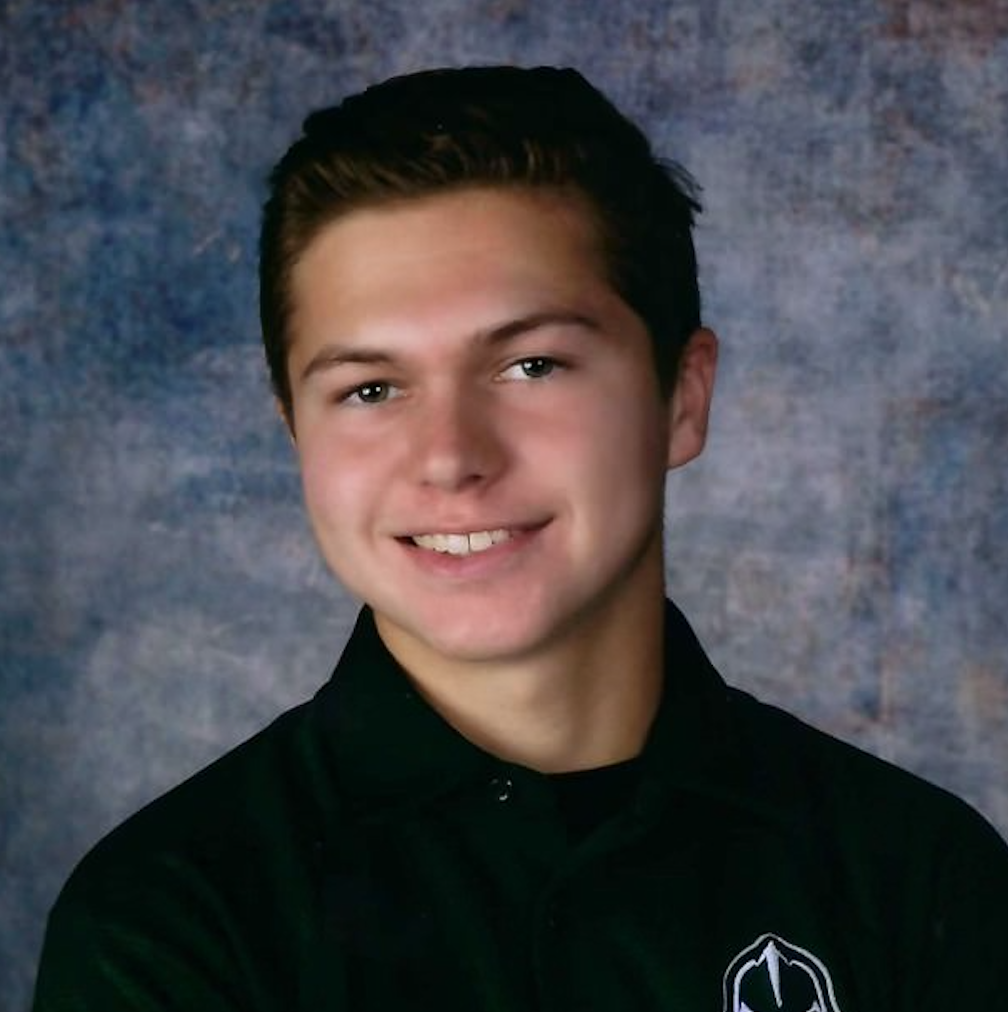 A headshot of a smiling person wearing a dark green polo shirt against a mottled blue-grey background.