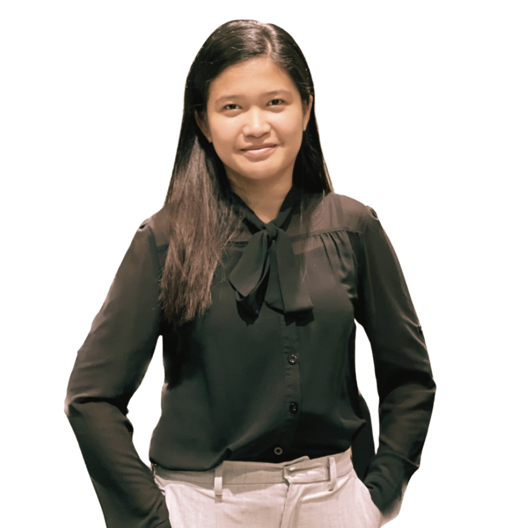 A person with long dark hair, wearing a black long-sleeved blouse with a tie neck and light pants, posing against a white.