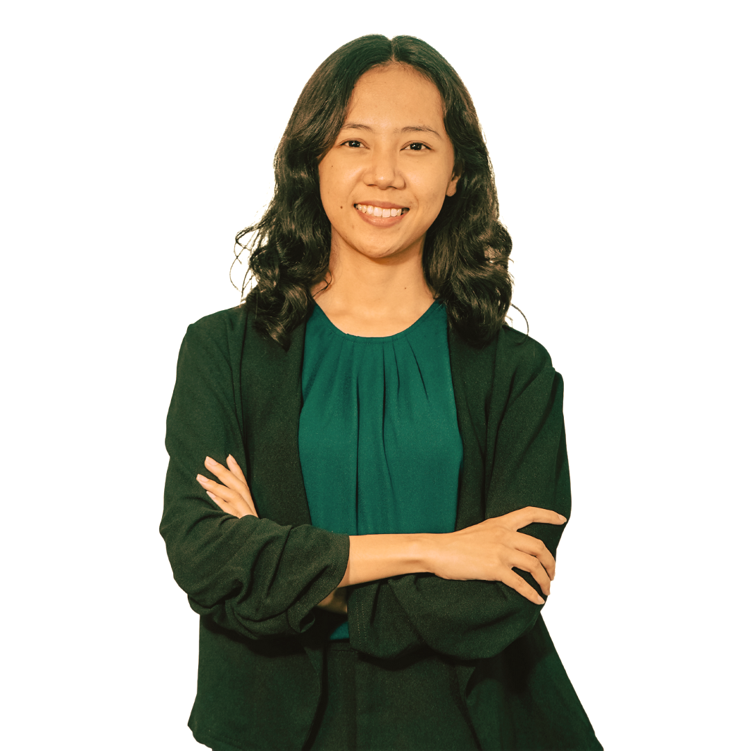 A person with long dark hair, wearing a green blouse and dark cardigan, stands with arms crossed against a white background.