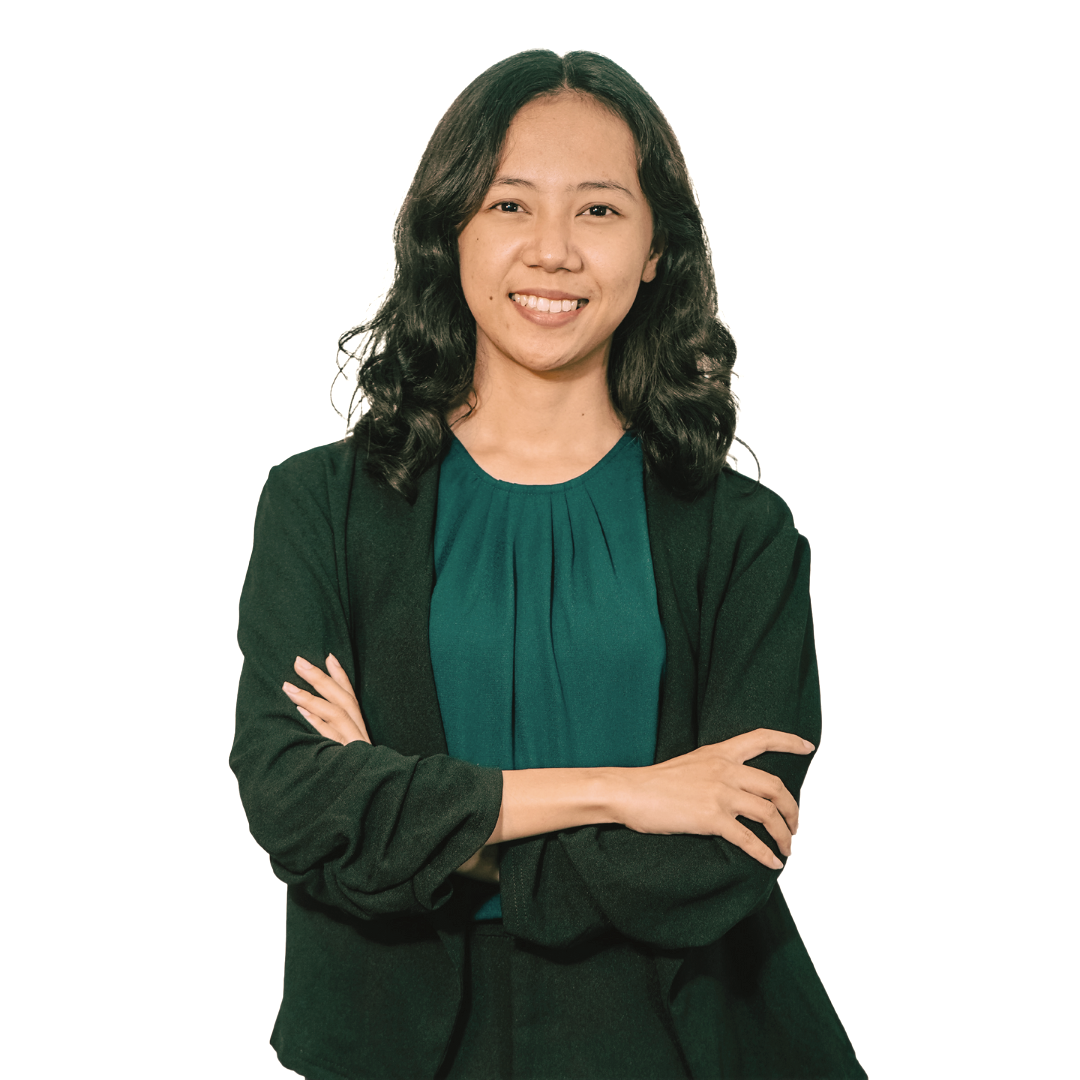 A smiling individual with dark wavy hair stands with arms crossed, wearing a dark green top under a black cardigan.