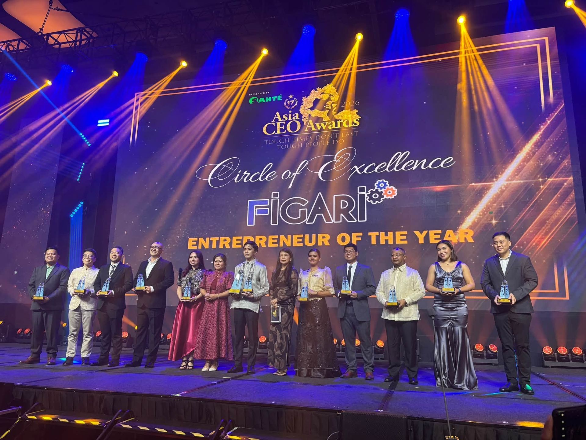 Award stage with a group of people holding trophies under colorful lights, “Entrepreneur of the Year” backdrop