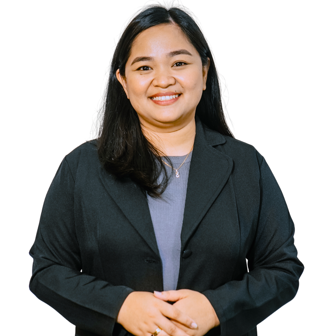 Woman with dark hair smiles, wearing a black blazer and gray shirt, hands clasped, studio setting.