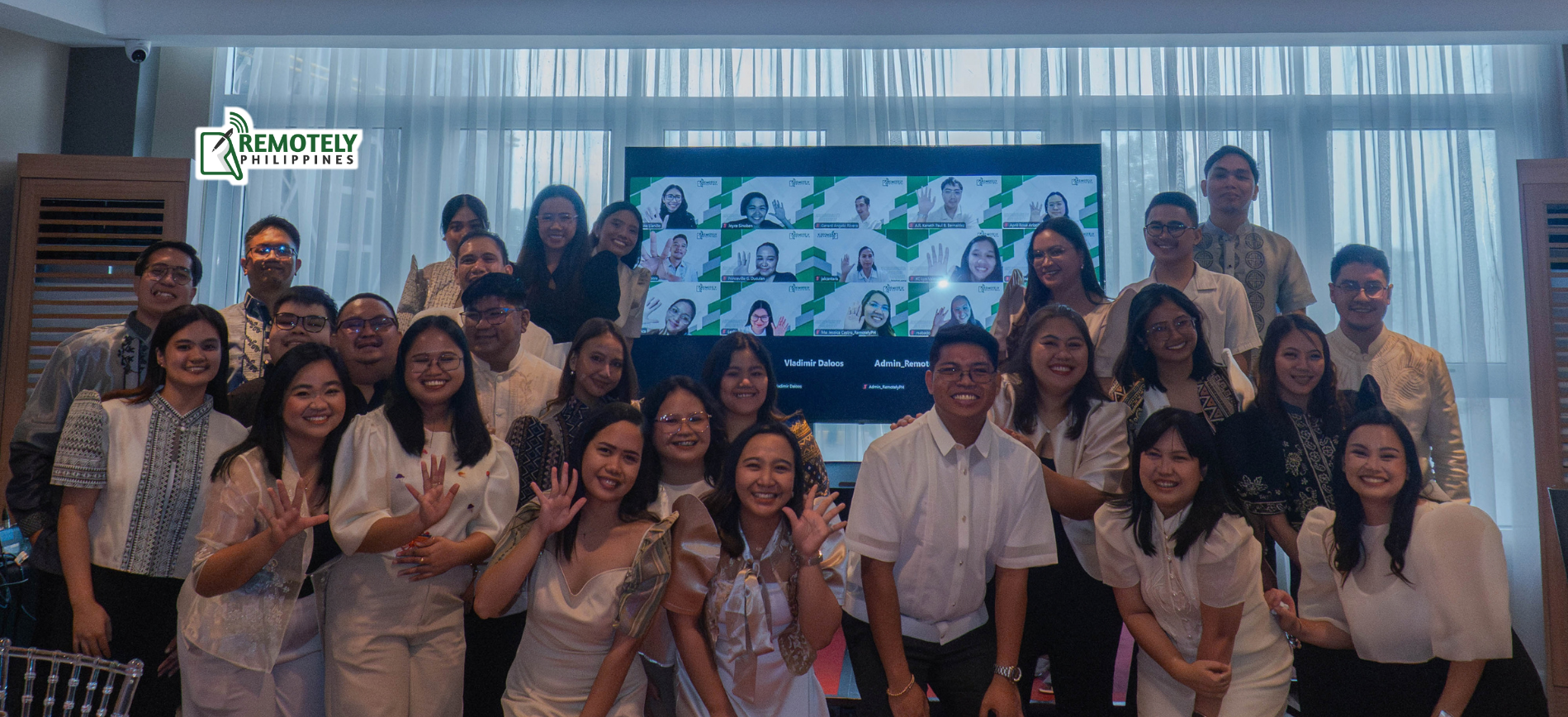 Group of people posing indoors for a photo in front of a large screen and curtains