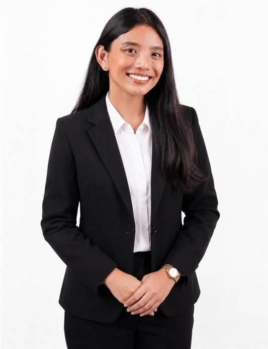 Woman in a light pink blazer over a blue shirt, standing and smiling against a white background