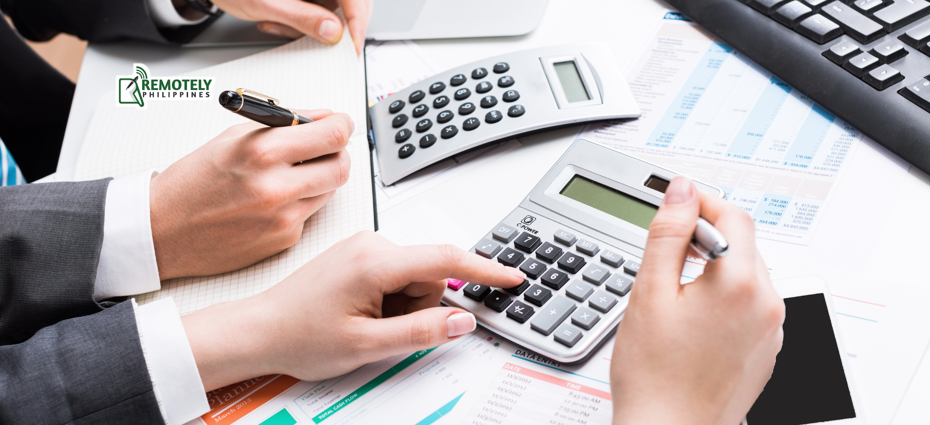 Hands calculating finances with calculators, paperwork, pens, and a keyboard on a desk.