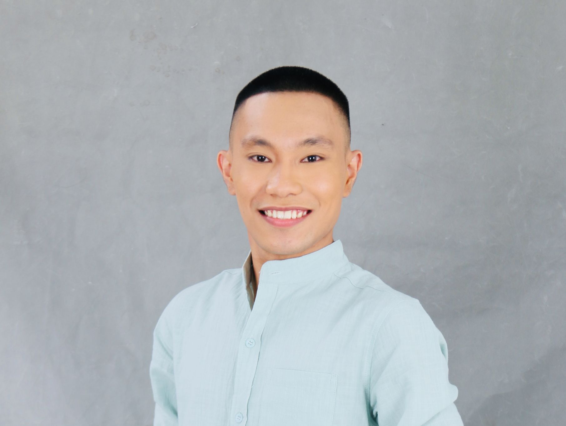A young man in a light blue shirt is smiling for the camera.