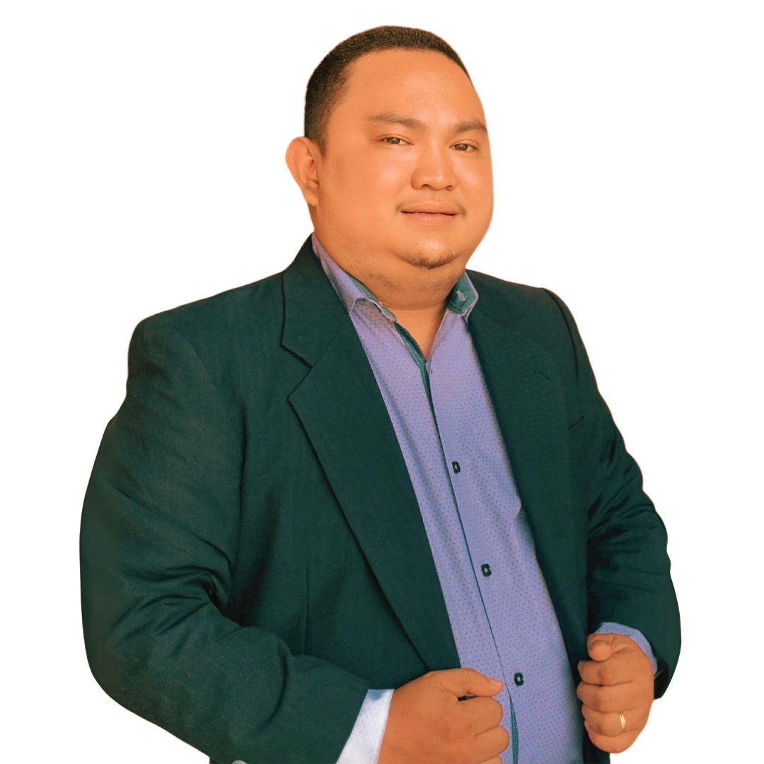 A person wearing a dark green blazer and light blue button-down shirt stands against a white background.
