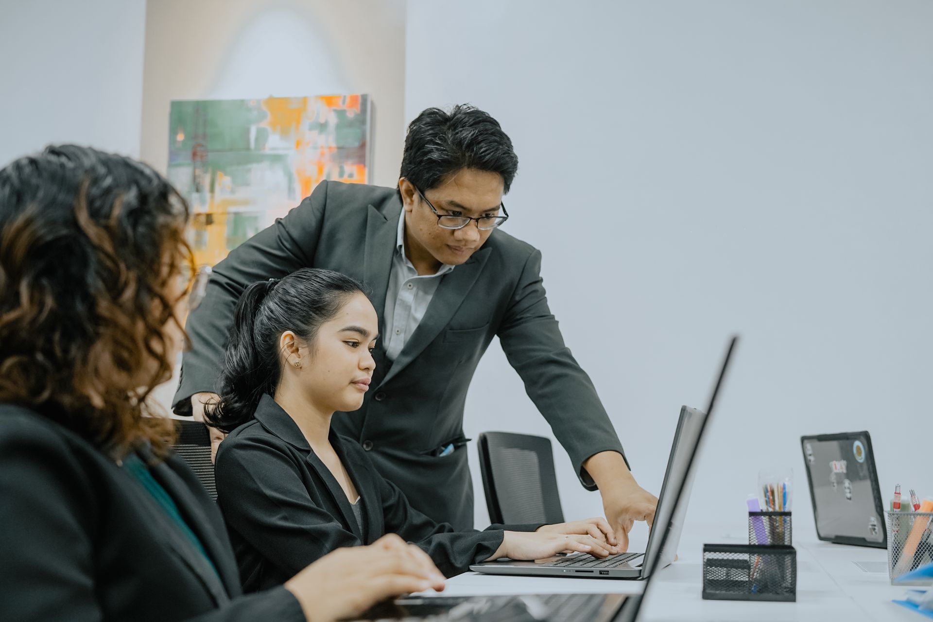 Three people in business attire in an office, one man pointing at a laptop.
