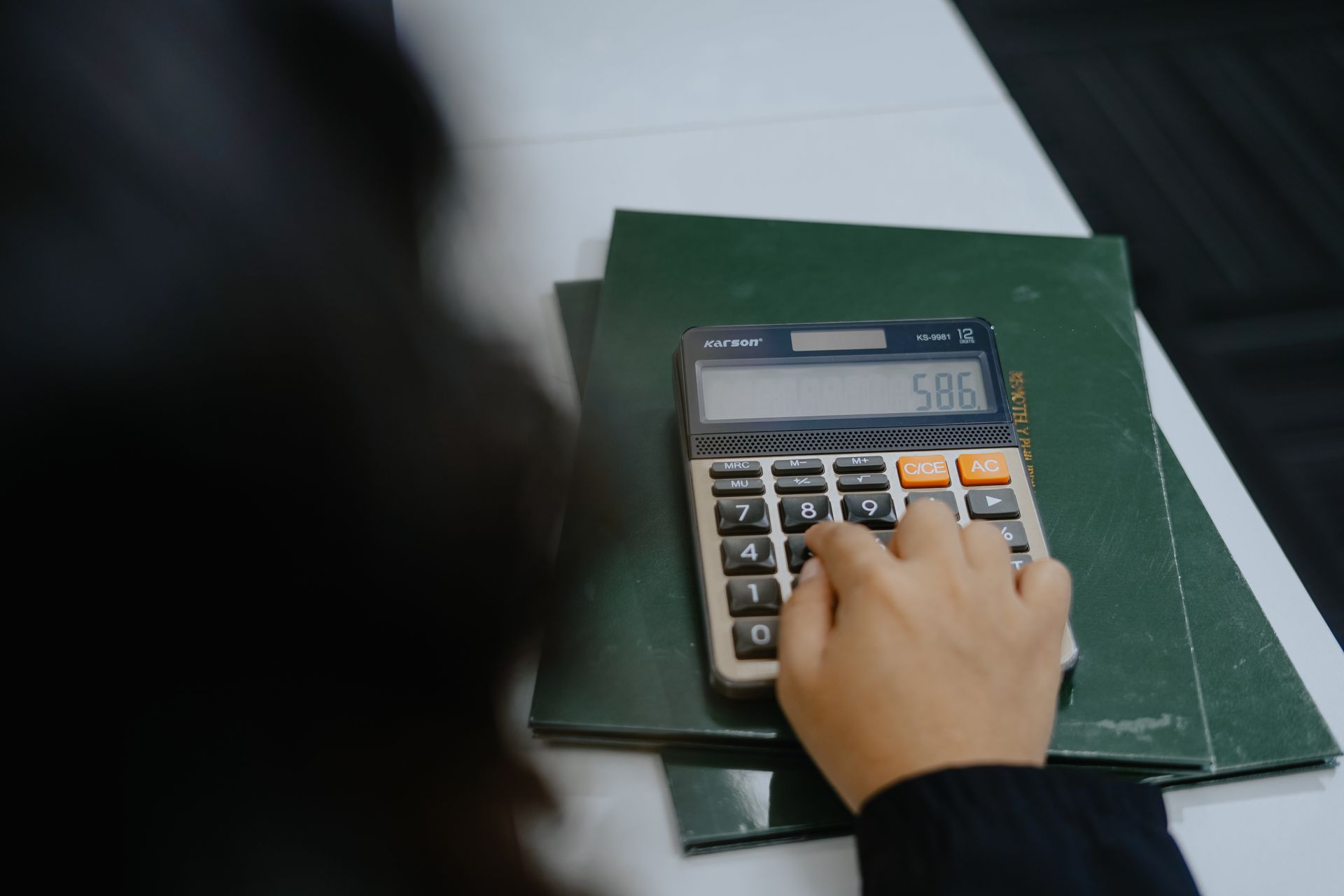 Hand pressing buttons on a calculator atop a green folder on a desk