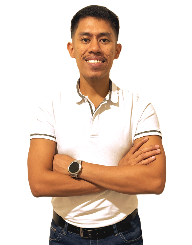 A person in a white polo shirt and dark jeans stands with arms crossed, wearing a watch and smiling against a white backdrop.