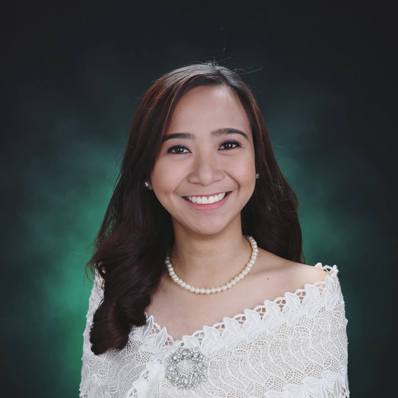 A woman wearing a white lace top and a pearl necklace smiles for the camera.