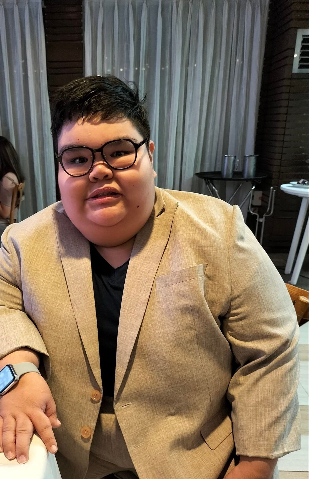A young man wearing glasses and a suit is sitting at a table.