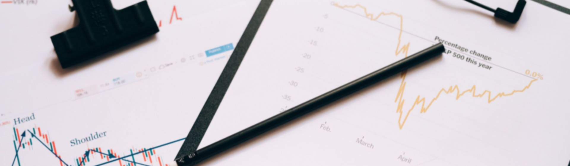Black pens on printed charts with colored line graphs and clipboards on a white desk