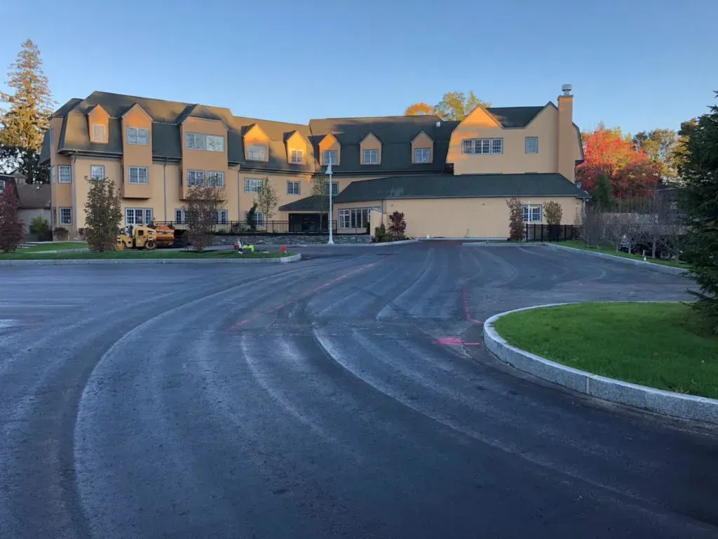 Large, yellow building with multiple dormer windows, surrounded by paved parking lot and grass.