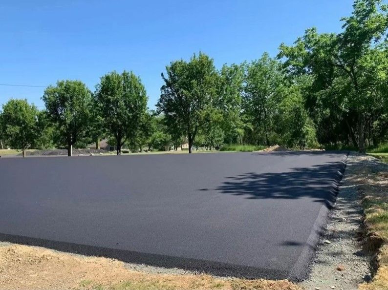 Freshly paved black asphalt lot beside trees under a clear blue sky