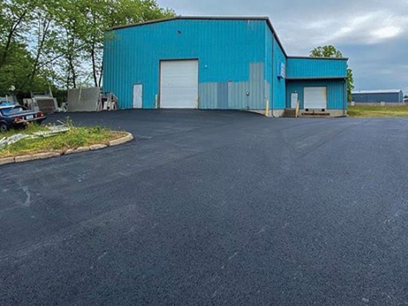 Blue industrial building with a newly paved black asphalt parking lot.