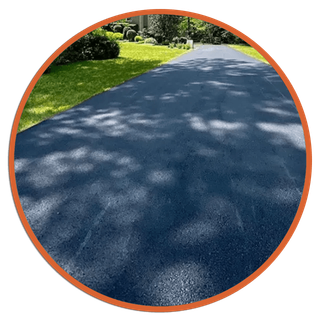 Black asphalt driveway with green grass on the side, under tree shadows.