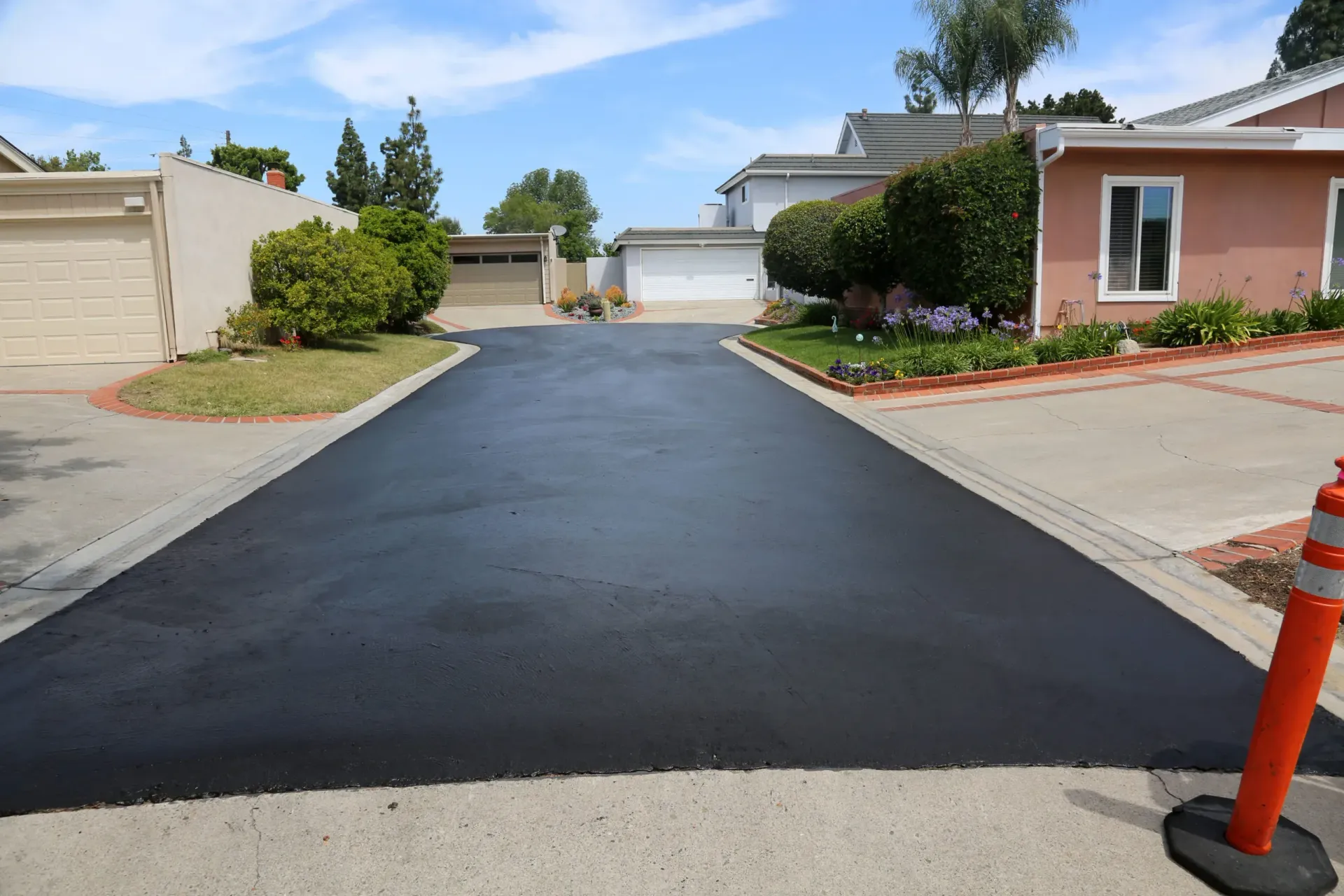 Freshly paved asphalt driveway in residential area, blue sky.
