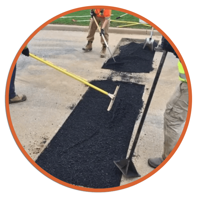 Workers spreading asphalt with rakes and shovels on a concrete road, repairing a damaged section.