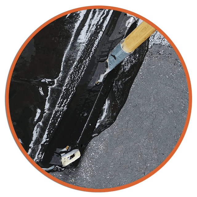 Close-up of black rubber tarp being cut with a utility knife on gray pavement