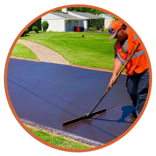 Worker in orange vest leveling fresh asphalt on a residential street.