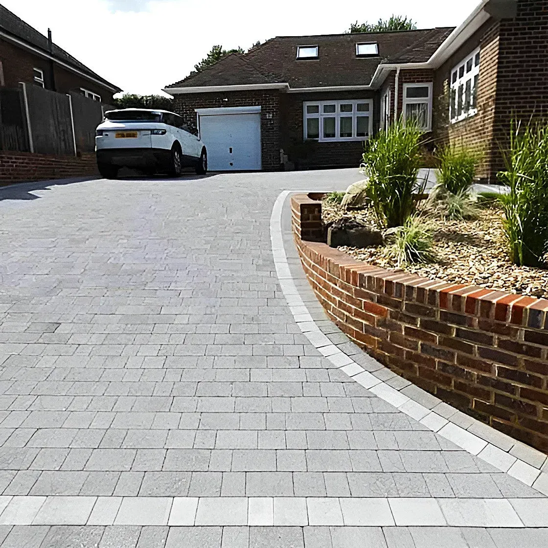 Gray brick driveway leading to a brick house with a white car parked in front.