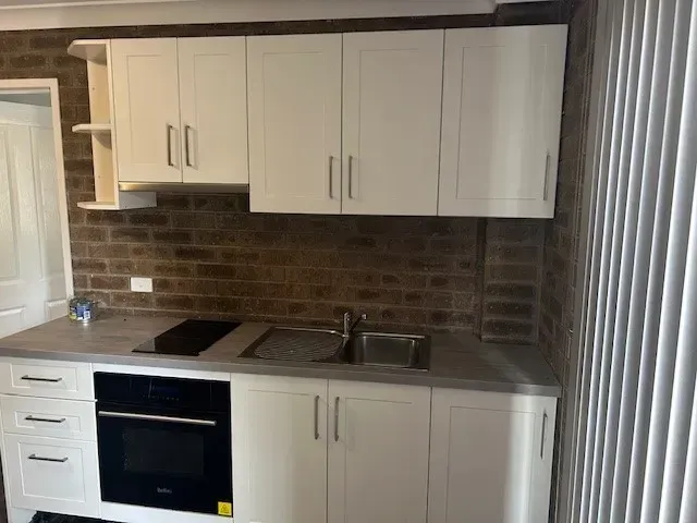 A kitchen with white cabinets and a brick wall